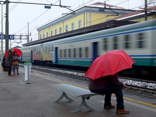 Immagine con treno, stazione, panchina, rosso, ombrello, binari, seduto, pioggia, ombrelli, uomo, binario, fili, numeri, viaggiatori