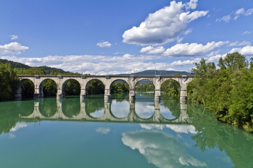Immagine con fiume, nuvole, ponte, archi, riflesso, acqua, cielo, verde, alberi, riflessi, montagne, arcate, pilastri, azzurro