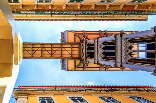 Immagine con finestre, cielo, ascensore, prospettiva, torre, nuvole, lisbona, giallo, passerella, azzurro, ponte, case, bifore, architettura, palazzi