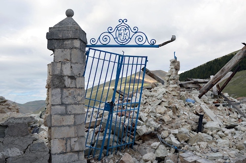 Immagine con cancello, rovine, colonna, pietre, cielo, macerie, travi, pilastro, ruderi, terremoto, ferro, rudere, azzurro, sassi, stemma, colline, nuvole, rotto, montagne
