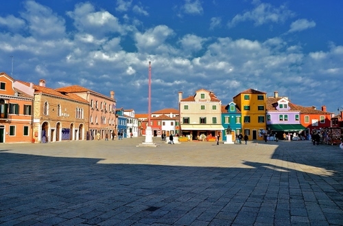 Immagine con piazza, nuvole, case, cielo, ombra, colori