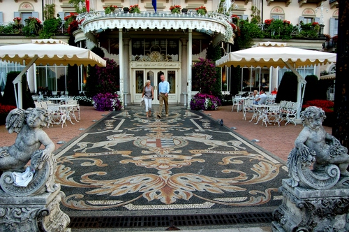 Immagine con statue, ombrelloni, sedie, persone, tavolini, fiori, ingresso, hotel, mosaico, tappeto, putti, albergo, coppia, stemma, liberty, porta, tavoli, due