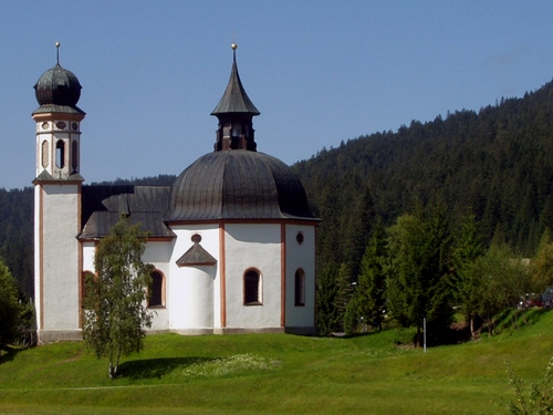 Immagine con chiesa, campanile, alberi, cupola, prato, montagna, bianco, verde, cielo