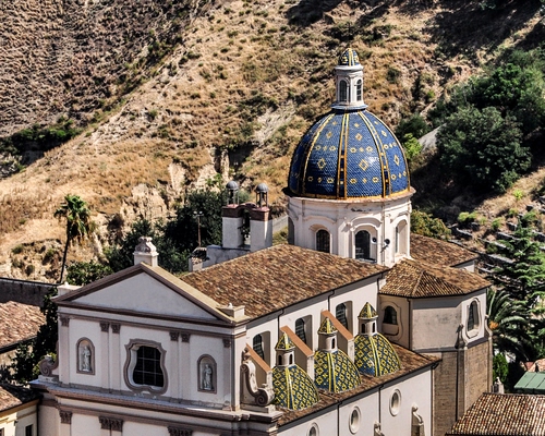Immagine con cupola, chiesa, tetto, alberi, blu, finestre, montagne, facciata