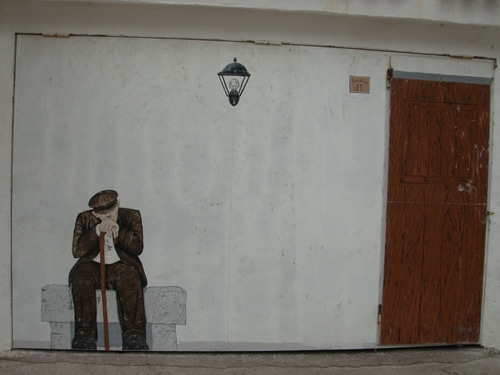 Immagine con porta, murales, bastone, uomo, vecchio, murale, panchina, muro, lampada, lampione, anziano