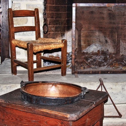 Immagine con sedia, camino, pentola, legno, cenere, catena, paiolo, paglia, brace, rame