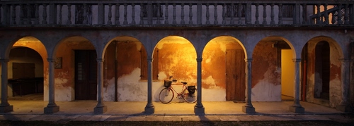 Immagine con archi, colonne, bicicletta, balaustra, portico, porte, luci, notte, notturno, portici, porticato, sera, ombre, bici, capitelli, finestre