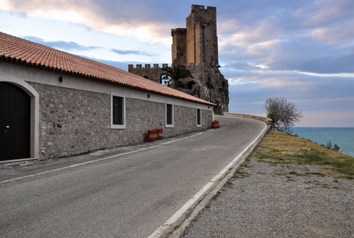 Immagine con strada, mare, castello, torre, cielo, nuvole, torri, albero, curva, rocca, casa