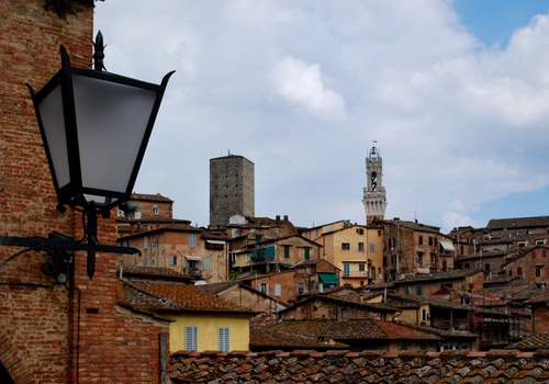 Immagine con lampione, tetti, campanile, torre, nuvole, panorama, case, scorcio, cielo, mattoni, tegole, torri