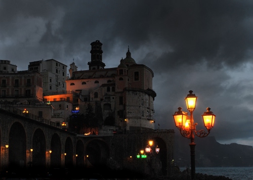 Immagine con nuvole, lampione, chiesa, archi, lampioni, luci, notte, mare, paese, campanile, notturno