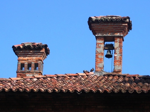 Immagine con tetto, campana, piccioni, cielo, tegole, comignolo, comignoli, coppi, campanella, azzurro, mattoni, campanile