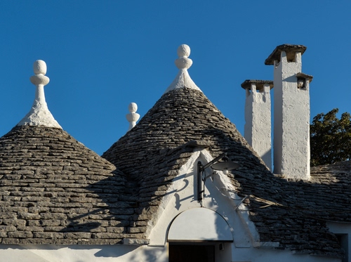 Immagine con trulli, tetti, bianco, comignoli, cielo, puglia, pietre, azzurro, alberobello, mattoni, pinnacoli, coni, camini