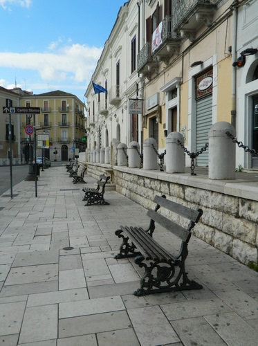 Immagine con panchine, strada, catene, palazzi, bandiera, catena, finestre, negozi, piazza
