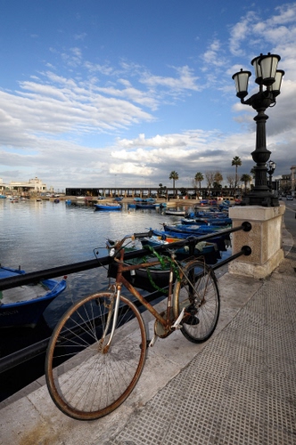 Immagine con bicicletta, barche, lampione, mare, cielo, porto, acqua, nuvole