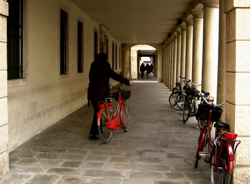 Immagine con colonne, finestre, biciclette, portico, persone, rosso, bicicletta, persona