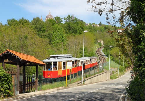 Immagine con strada, lampioni, treno, rosso, alberi, binari, tettoia, verde, cielo, stazione, trenino, rotaie, bianco, vagoni, tetto, tram, chiesa, ferrovia