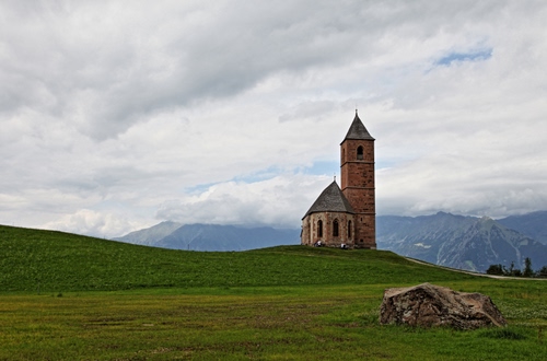Immagine con chiesa, campanile, nuvole, prato, verde, paesaggio, montagna, cielo, montagne