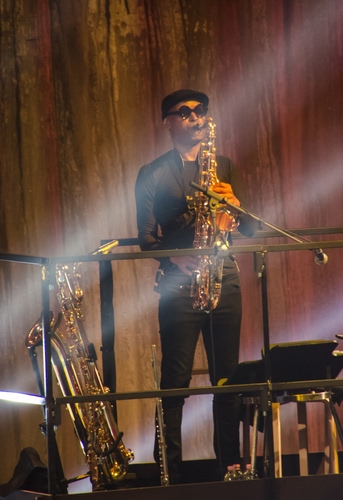 Immagine con occhiali, strumenti, musicista, microfono, ottoni, luci, musica, nero, uomo, sassofono, suonatore, palco, berretto, sax, cappello, raggi, basco, ottone, luce, artista, oro, concerto