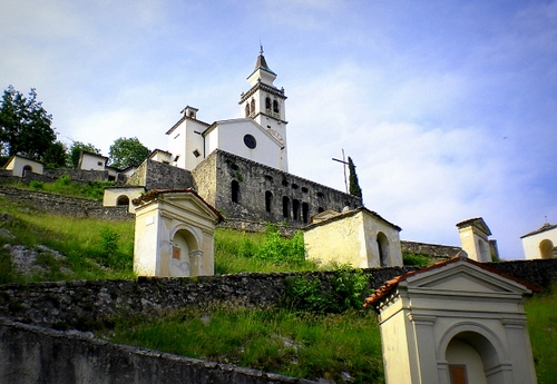 Immagine con chiesa, campanile, verde, cielo, croce, cappelle, archi, nuvole, erba, alberi, muro, muretti, finestre, croci, cimitero, salita, edicole
