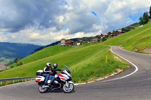 Immagine con strada, nuvole, cielo, moto, montagna, motociclisti, curva, case, motocicletta, due, verde, caschi, alberi, curve, ruote, asfalto, guardrail, prati, erba, prato, paese, tornante