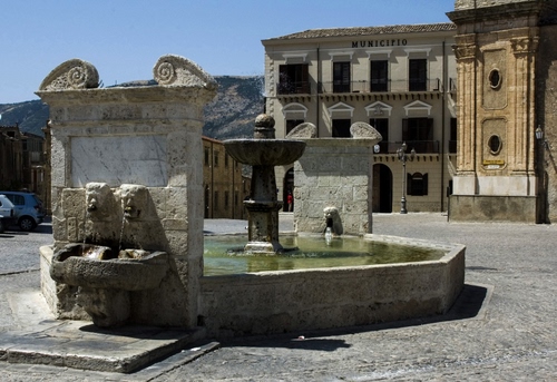 Immagine con fontana, piazza, acqua, finestre, municipio, palazzi, case, cielo, vasca, pietra, zampilli, porte, ombra
