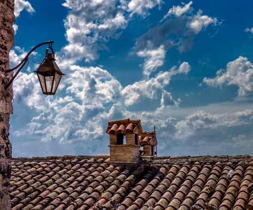 Immagine con nuvole, cielo, tetto, lampione, comignoli, tegole, muro, coppi, azzurro, lampada, lampadina, comignolo, tetti