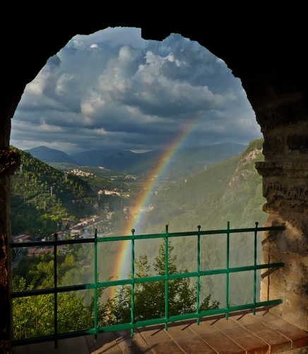 Immagine con nuvole, arcobaleno, arco, cielo, ringhiera, montagne, alberi, panorama, affaccio, iride, paesaggio, inferriata, verde, ferro, case, belvedere, mattoni, valle