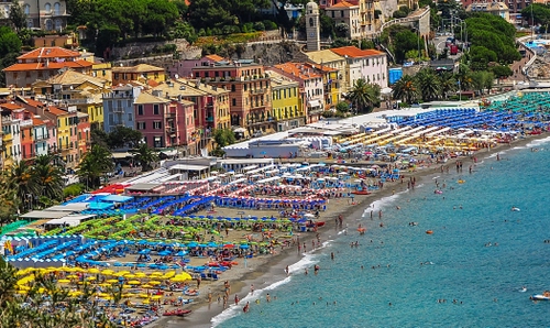 Immagine con ombrelloni, mare, spiaggia, case, alberi, campanile, acqua, bagnanti, estate, verde, colori, giallo, persone, chiesa, palazzi, azzurro, paese