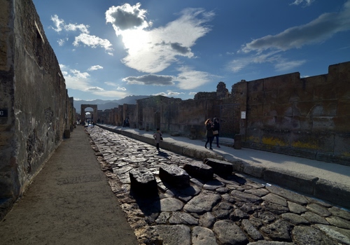 Immagine con nuvole, strada, cielo, pietre, lastricato, via, prospettiva, azzurro, muri, arco, rovine, persone, pietra, marciapiede, turisti, scavi, passanti, archi, resti, pompei, archeologia, ombre