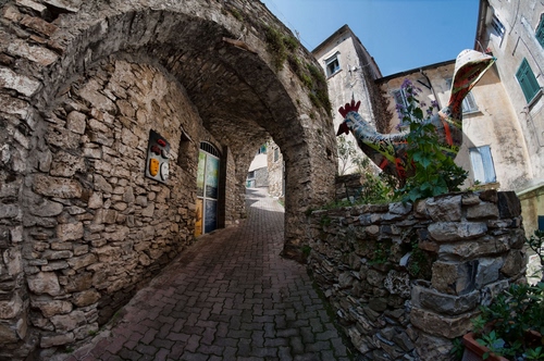 Immagine con arco, gallo, finestre, pietre, vicolo, porta, cielo, strada, scorcio, case, azzurro, maschere, pietra, piante, verde, scultura, borgo, salita