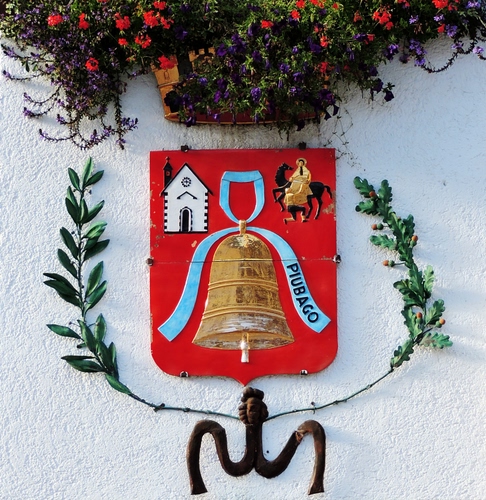 Immagine con stemma, rosso, fiori, campana, rami, nastro, chiesa, azzurro, verde, muro, piante, scritta, cavallo, cavaliere, pianta, foglie, bianco, santo