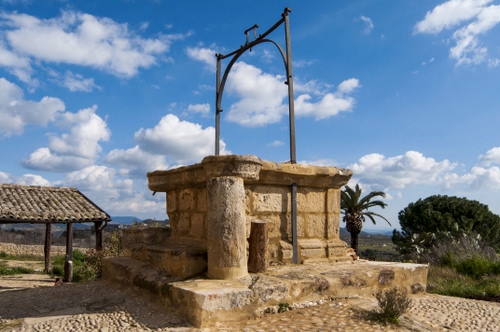 Immagine con pozzo, cielo, nuvole, palma, alberi, verde, tettoia, tetto, azzurro, arco, pietra, coppi, tegole, piante, antico, bianco, sassi, ferro