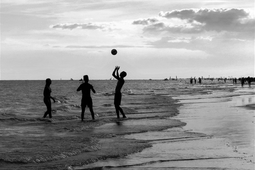 Immagine con mare, spiaggia, bianconero, nuvole, persone, palla, gioco, acqua, controluce, cielo, sabbia, battigia, nero, giocare, onde, bagnasciuga, ragazzi, bagnanti, pallone, silhouette